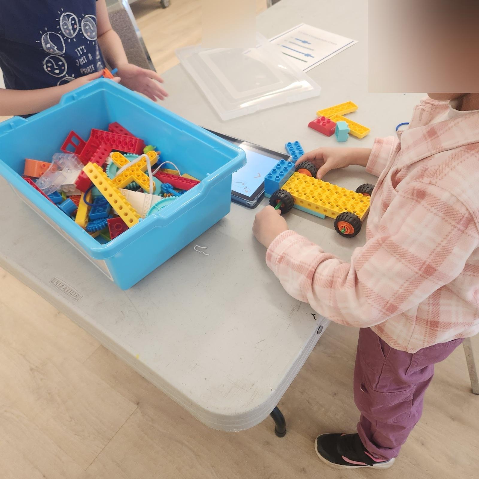 Une enfant construit une voiture en briques pendant un atelier
